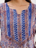 An intricately designed fabric with a mix of paisley and geometric patterns in vibrant colors. The top features vertical blue panels with crisscross white lacing and decorative sequins. The fabric has a colorful combination of red, orange, and white accents.