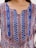An intricately designed fabric with a mix of paisley and geometric patterns in vibrant colors. The top features vertical blue panels with crisscross white lacing and decorative sequins. The fabric has a colorful combination of red, orange, and white accents.