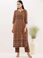 A vibrant printed kurti in rich peacock green and gold hues displayed on a minimalist white mannequin.
