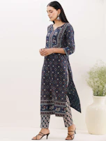 A model wearing a deep navy blue abaya with subtle gold accents standing against a minimalist cityscape.