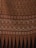 The image displays a fabric or textile with intricate patterns. The upper portion features repetitive floral motifs in red on a beige background. Below it, there is a segment with zigzag patterns in shades of brown. This is followed by a section with symmetrical, ornamental designs in beige and dark brown. The bottom-most part showcases vertical elements, resembling leaves or feathers, in red and black.