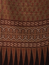 The image displays a fabric or textile with intricate patterns. The upper portion features repetitive floral motifs in red on a beige background. Below it, there is a segment with zigzag patterns in shades of brown. This is followed by a section with symmetrical, ornamental designs in beige and dark brown. The bottom-most part showcases vertical elements, resembling leaves or feathers, in red and black.