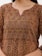 Intricate and vibrant textile design featuring an olive green background with red and cream floral and geometric patterns. The fabric includes small embroidered floral motifs and circular designs, creating a rich, detailed texture. The neckline has a subtle V-shape, bordered with red stitching.