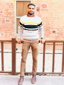 A stylish man wearing a cozy knit sweater standing against a brick wall.