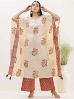 An elegant cream anarkali suit with delicate floral patterns, hanging in a softly lit boutique.