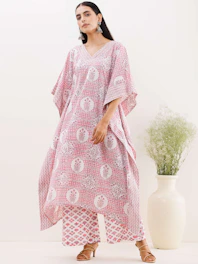 Confident plus-size woman in a flowing blush pink kaftan, smiling warmly against a soft beige background.