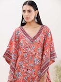 A person with long black hair wearing large jhumka earrings and a colorful garment featuring floral patterns in shades of red, blue, and white. The garment has a V-neck design with intricate patterns along the neckline and sleeves.