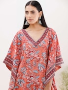 A person with long black hair wearing large jhumka earrings and a colorful garment featuring floral patterns in shades of red, blue, and white. The garment has a V-neck design with intricate patterns along the neckline and sleeves.