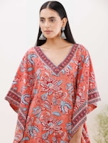 A person with long black hair wearing large jhumka earrings and a colorful garment featuring floral patterns in shades of red, blue, and white. The garment has a V-neck design with intricate patterns along the neckline and sleeves.