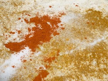 A close-up view of scattered orange and yellow powders on a white surface. The colorful powders are spread unevenly, creating a textured and dynamic contrast against the background.