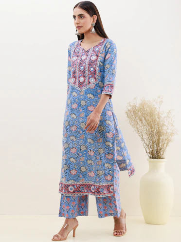 A graceful woman modeling a printed kurti adorned with peacock-inspired patterns in deep greens and golds.