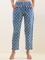 A person wearing blue floral-patterned pants and clear sandals. The pants have an elastic waistband with a drawstring and feature a repeating pattern of green and white flowers.