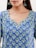 A woman wearing a blue kurta featuring a floral pattern with green and white accents. She has long hair and is wearing large, ornate earrings with a gold finish and turquoise beads.
