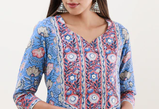 A person is wearing a blue floral-patterned kurta with intricate designs in shades of blue, red, and white. The attire has a v-shaped neckline and three-quarter-length sleeves. They are accessorized with large, ornate, silver jhumka earrings. The hair is styled straight and parted in the middle.