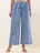 A pair of wide-legged pants featuring an intricate, symmetrical pattern design in blue with darker and lighter contrasts. The fabric gives a casual yet sophisticated appearance, and the pants are paired with clear, modern-looking heeled sandals. The background is a neutral shade, highlighting the pants.