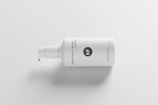 A white plastic pump bottle with minimalist design elements lies on its side against a plain white background. The bottle has black text printed vertically on its surface, highlighting branding and product details.
