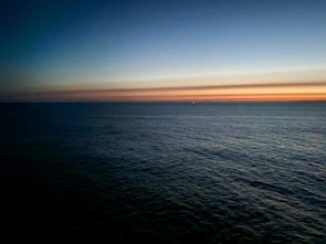 Wide-angle view of a calm open sea under a warm terracotta sky at sunset.