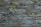 A tightly fitted stone wall made of irregularly shaped, flat pieces of slate arranged horizontally. The color palette includes various shades of gray, with subtle hints of green and brown, and the surface texture is rugged and natural.