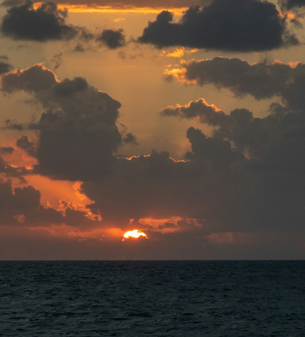 the sun is setting over the ocean on a cloudy day