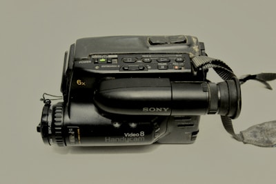 A vintage Sony Handycam camcorder featuring various control buttons and a strap. The camcorder is equipped with a video lens and marked with 'Video8' and '6x' on the side. It has a slightly worn exterior, indicating frequent use.