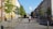 A cyclist rides down a dedicated bike lane on a tree-lined urban street, flanked by buildings with classic architecture. Cars are parked along the side, and small green trees enhance the sidewalk, contributing to the orderly and peaceful city environment.