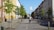 A cyclist rides down a dedicated bike lane on a tree-lined urban street, flanked by buildings with classic architecture. Cars are parked along the side, and small green trees enhance the sidewalk, contributing to the orderly and peaceful city environment.
