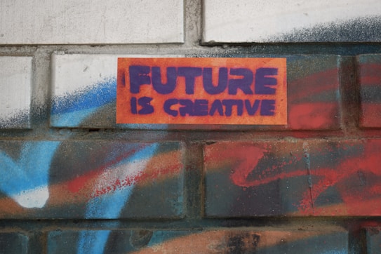 A brick wall features graffiti-style text that reads 'FUTURE IS CREATIVE' in bold purple letters against an orange background. Surrounding the text are vibrant spray-painted patterns in shades of blue, red, and white, providing a colorful and artistic backdrop.
