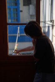 Person standing peacefully next to a sleek aluminum acoustic window frame, sunlight filtering softly through.