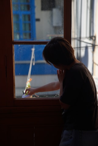 Person standing peacefully next to a sleek aluminum acoustic window frame, sunlight filtering softly through.