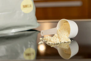 Fresh vanilla whey protein powder spilling gently from a scoop onto a wooden surface.