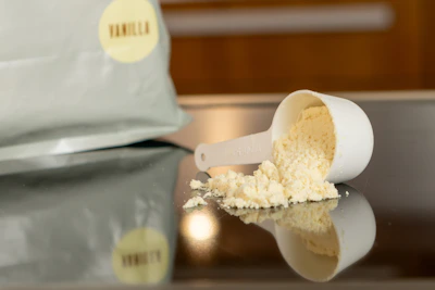 A vibrant close-up of a scoop of creamy vanilla whey protein powder spilling gently onto a rustic wooden surface.
