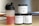 There are three supplement containers and a shaker bottle. One container is labeled 'PRE-WORKOUT' with a lightning bolt symbol, another is labeled 'CREATINE' with a chemical structure diagram, and the third is labeled 'PROTEIN' with an icon of a flexing arm. The shaker bottle contains a red liquid.