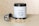 A container of protein powder with a white label displaying the word 'PROTEIN' and an icon of a flexed arm. The container has a black lid and is placed on a flat surface. In front of it, there is a scoop partially filled with the powder, some of which is spilled on the surface.