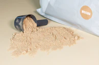 Powdered carob flour spilling gently from a burlap sack onto a wooden surface.