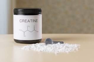 a bottle of creatine next to a spoon on a table