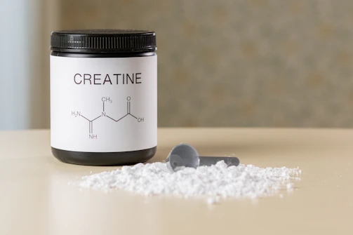 a bottle of creatine next to a spoon on a table