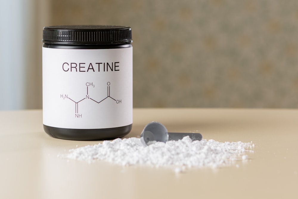 a bottle of creatine next to a spoon on a table