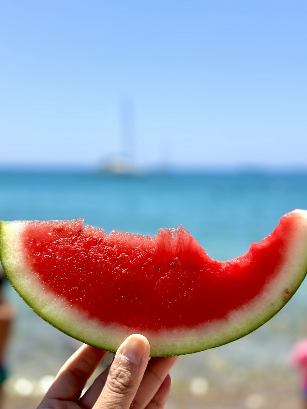 a person holding a slice of watermelon on a beach