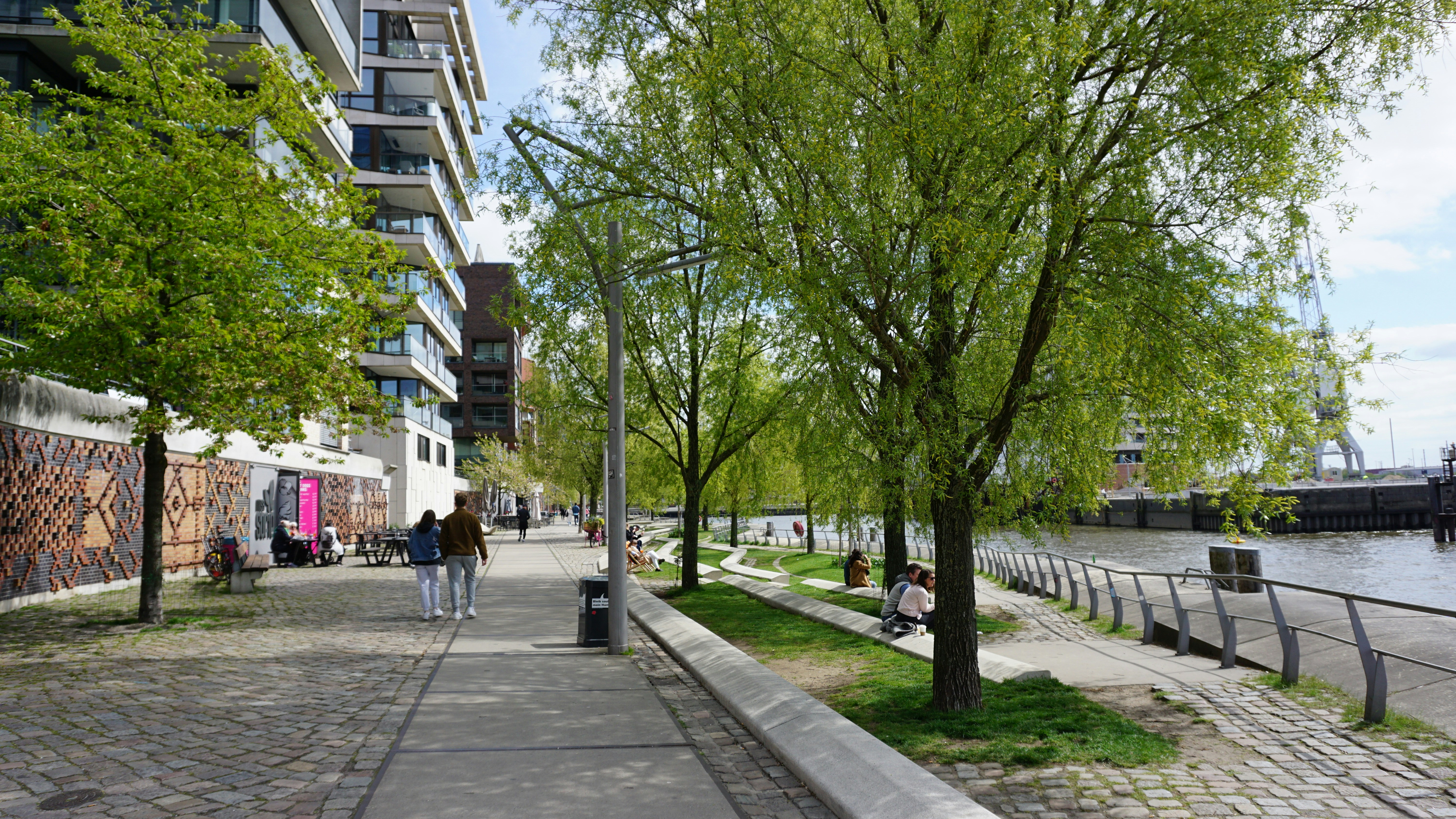 a couple of people walking down a sidewalk next to a river