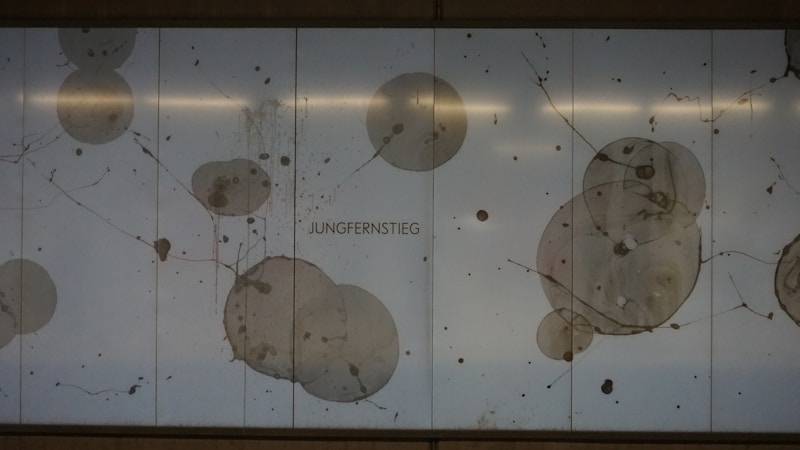 Circular patterns and splatters resembling abstract art are displayed on a light background with the word 'JUNGERNSTIEG' in the center. The design features various shades of gray and brown, creating a modern and minimalist aesthetic.