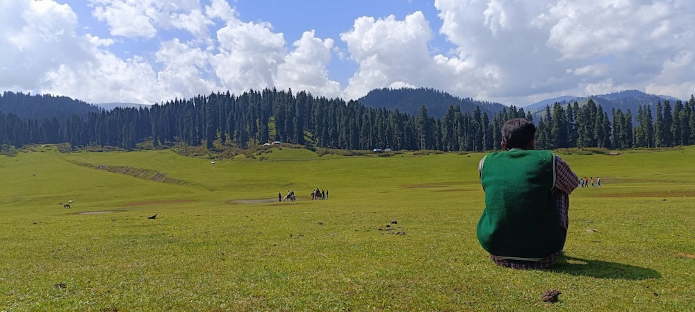 a man sitting on a green field flying a kite