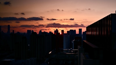An artistic cityscape at dusk with warm orange and red tones illuminating the skyline