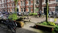 Urban delivery scene with bicycles and electric vans moving through a leafy green city street.