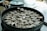 A large metal steamer filled with neatly arranged dumplings, each with a crinkled appearance, indicating they are ready to be cooked or recently cooked. The background displays various kitchen items including a light blue pot, suggesting a culinary setting.