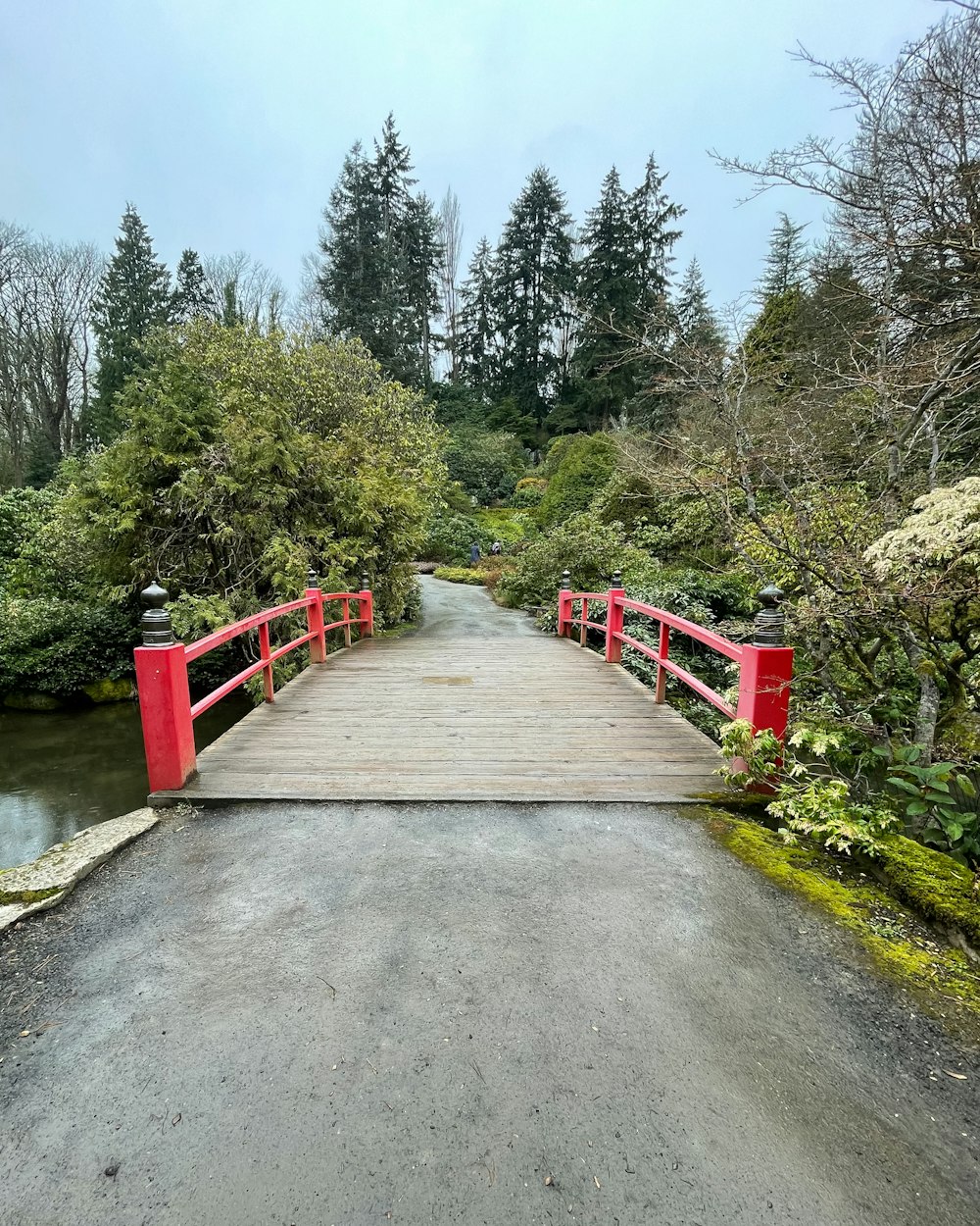 a red bridge over a small stream in a park