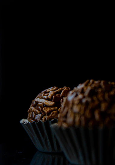 Close-up of a glossy, gold-dusted chocolate truffle resting on black velvet.