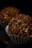 Two chocolate truffle candies with a textured coating of chocolate pieces are presented in silver cupcake liners against a dark background.