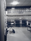 A clinical waiting area with a row of empty chairs against a wall decorated with geometric patterns. A wheelchair is parked to one side, and the lighting is soft and subdued. The setting seems orderly and quiet with a sterile ambiance.