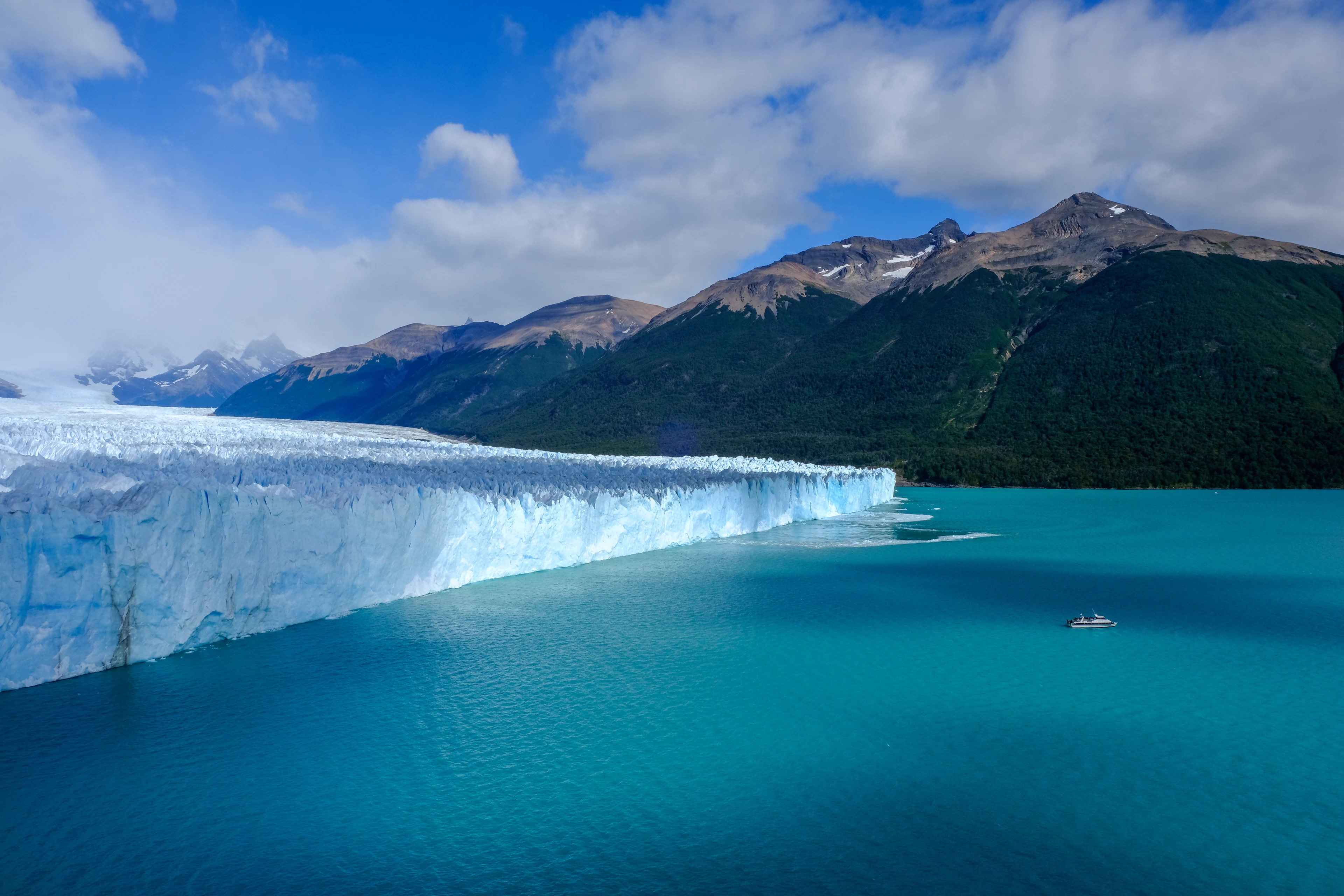 A small boat on turquoise water before the wall of the Perito Moreno Glacier, Argentina
