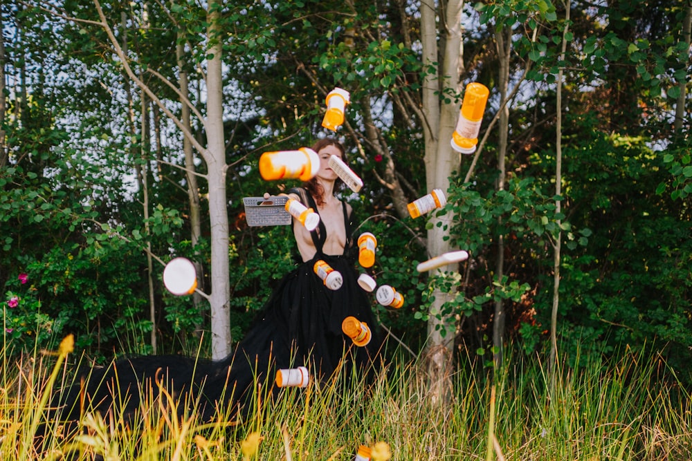eine Frau in einem schwarzen Kleid, die mit orangefarbenen und weißen Flaschen jongliert